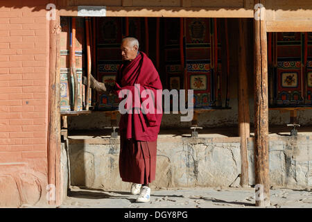 Un monaco tibetano in parte anteriore del legno ruote della preghiera che circonda il monastero, Kora, del Tibetano monastero Labrang, Xiahe, Gansu Foto Stock