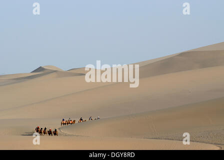 Camel caravan con i turisti di fronte le dune di sabbia del deserto del Gobi durante la salita del monte Mingshan vicino a Dunhuang Foto Stock