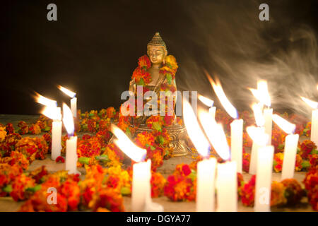 Una figura del Buddha Shakyamuni è decorata con ilo o ghirlande ed è circondata da candele accese Foto Stock