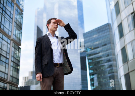 Giovane uomo d affari guardando avanti sui grattacieli sullo sfondo Foto Stock