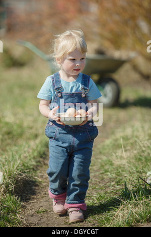 Agricoltore ragazza portando una ciotola di uova Foto Stock