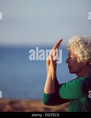 Vecchia donna stretching le braccia dal mare. Senior donna caucasica esercitando sulla spiaggia di mattina. Fitness e uno stile di vita sano Foto Stock