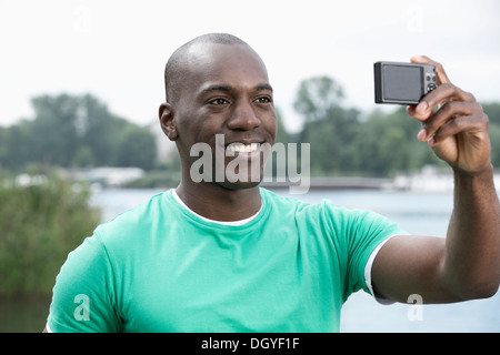 Uomo sorridente tenendo fotografia di se stesso dal lago Foto Stock