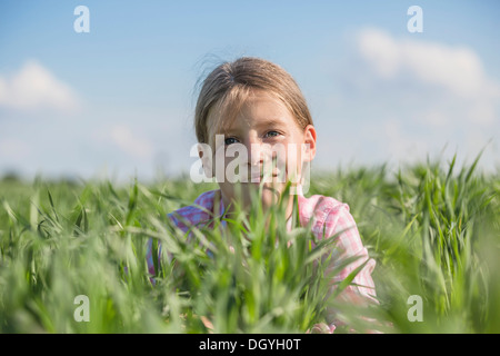 Una giovane ragazza sorridente giacente in erba su un giorno d'estate Foto Stock