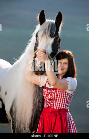 Giovane donna che indossa un vestito con grembiule cuddling con uno zingaro Vanner o Tinker cavallo, pinto, bianco e nero, Tirolo del nord, Austria, Europa Foto Stock