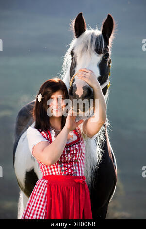 Giovane donna che indossa un vestito con grembiule cuddling con uno zingaro Vanner o Tinker cavallo, pinto, bianco e nero, Tirolo del nord, Austria, Europa Foto Stock