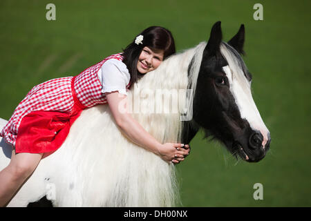 Giovane donna che indossa un vestito con grembiule seduta senza una sella o briglia e coccole con una zingara Vanner o Tinker cavallo, Pinto Foto Stock