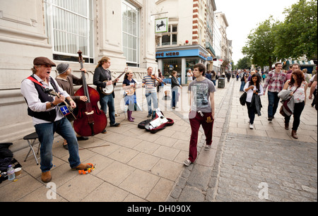 Le persone camminare davanti a un folk band musicista di strada per strada, Norwich, Norfolk, Regno Unito Foto Stock