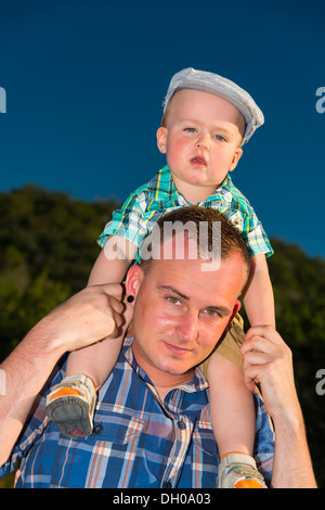 Giovane maschio bambino seduto sulle spalle di suo padre godendo la corsa. Foto Stock