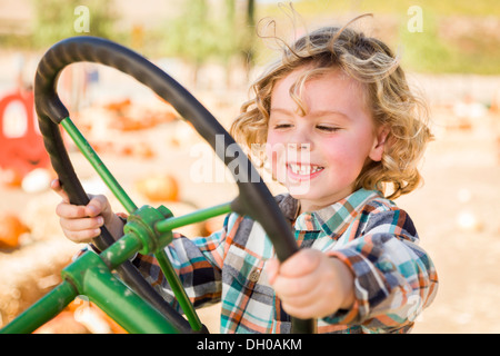 Adorable del giovane ragazzo giocando su un vecchio trattore in un rustico Outdoor rientrano l'impostazione. Foto Stock