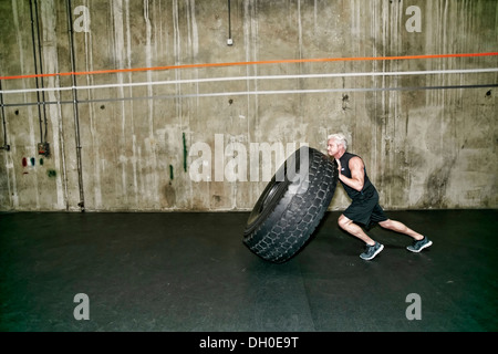 Razza mista uomo grande spinta pneumatico in palestra Foto Stock