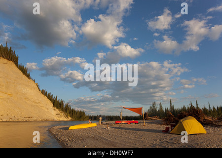 Camp con tenda e tarp su una barra di ghiaia, alta cut bank dietro, superiore Liard river, Yukon Territory, Canada Foto Stock