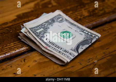 Bundle ripiegata di ben utilizzato dollar note su un usurato bar in legno. Foto Stock