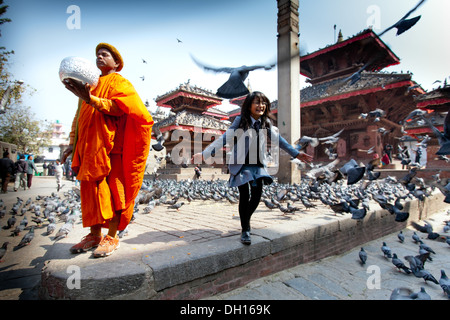 Un Sadhu Uomo Santo si erge con le sue donazioni ciotola come una bambina corre attraverso i piccioni, Kathmandu Durbar Square, Nepal Foto Stock