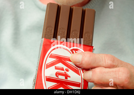 Donna anziana mangiando un Fairtrade 4 dito Kit Kat biscotti al cioccolato Foto Stock