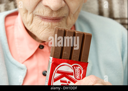 Donna anziana mangiando un Fairtrade 4 dito Kit Kat biscotti al cioccolato Foto Stock