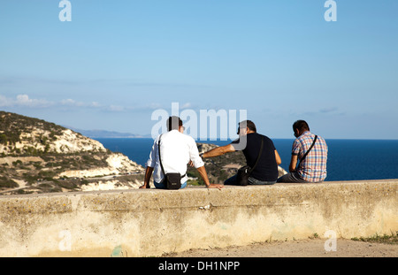 Gli uomini seduti sulla parete dal faro di Capo Sant'Elia a San Bartolomeo guardando sopra Calamosca Bay - Sardegna Foto Stock