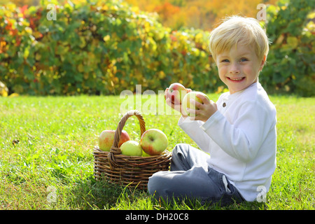 Un sorridente bambina è in possesso di due pezzi di frutta nelle sue mani come egli siede in erba presso un Apple orchard in una giornata di sole Foto Stock