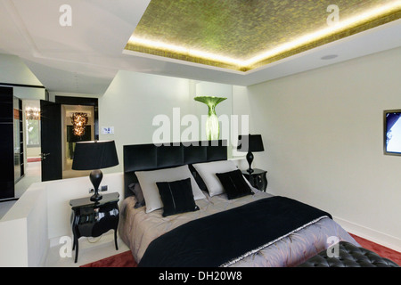 Incassato, oro illumina il soffitto sopra il letto con testiera in pelle nera e nero piegato buttare in camera da letto moderna Foto Stock
