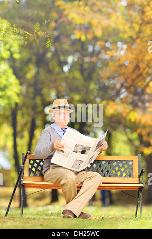 Senior gentleman seduto su una panchina leggendo un giornale in un parco in autunno Foto Stock