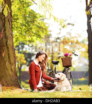 Bella donna seduta su un prato verde e guardando il suo labrador retriever cane in un parco Foto Stock