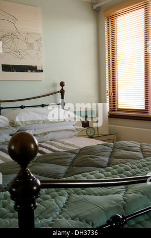 Un piccolo ma ben progettato camera da letto matrimoniale con un pallido pareti blu, tende a strisce, modellato quilt/piumone e cuscini bianchi. Foto Stock