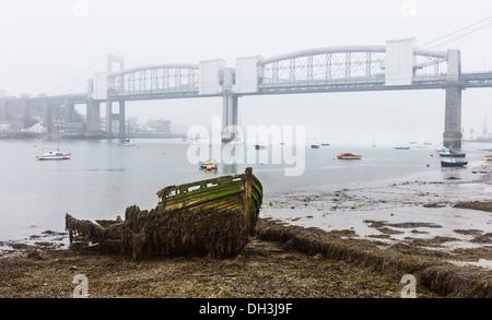 Marciume barca sulla banca del fiume Tamar con Royal Albert Bridge come sfondo su una mattinata nebbiosa a Plymouth, Devon UK. Foto Stock