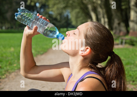 Attraente donna sportiva acqua potabile da una bottiglia dopo il jogging o in esecuzione Foto Stock