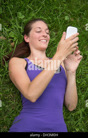 Giovane donna felice sdraiati su un prato verde è utilizzando uno smartphone Foto Stock