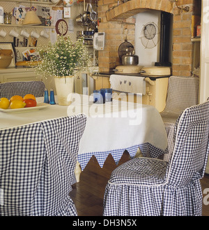 Cottage cucina con blue+white controllato copre allentato su sedie a tavola con un panno bianco con abbinamento di rivestimento del controllo Foto Stock