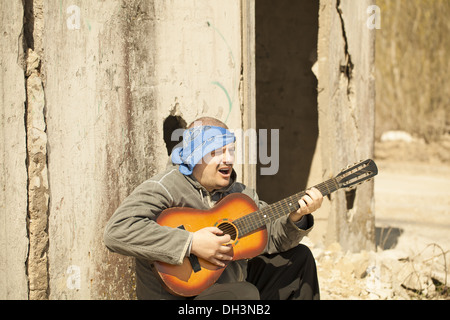 Uomo a suonare la chitarra appoggiata contro la parete Foto Stock