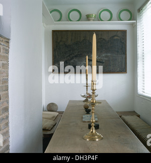 Green refilato piastre su scaffale alto sopra la pittura nella piccola sala da pranzo con alti candelieri in ottone sulla tabella semplice con panchine Foto Stock