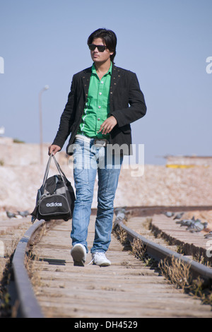 Uomo in blue jeans camicia bicchieri sacchetto contenitore camminando sul binario ferroviario Foto Stock