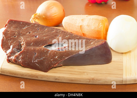 Un pezzo di carne di manzo crudo fegato con verdure sul bordo di taglio Foto Stock