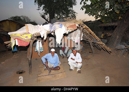 Famiglia tribale seduta al di fuori della loro capanna, tribù Bhil, Madhya Pradesh, India Foto Stock