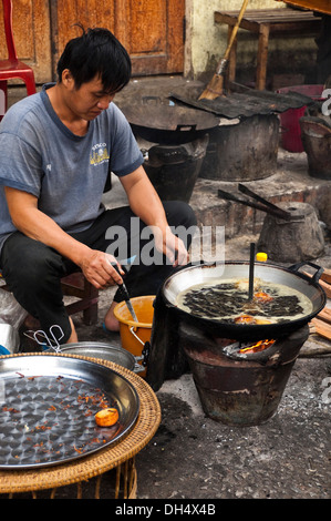 Ritratto verticale di un uomo Lao friggere piccole ciambelle in un wok sul ciglio della strada. Foto Stock