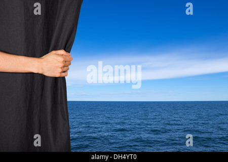 Apertura a mano tenda nera con mare e cielo blu dietro di esso. Foto Stock