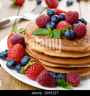 Pila di Pancake fatti in casa con fragole lamponi e mirtilli sulla piastra bianca Foto Stock