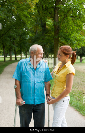 Una donna e un uomo anziano con le stampelle passeggiando nel parco Foto Stock