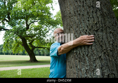 Felice uomo anziano abbracciando un albero Foto Stock