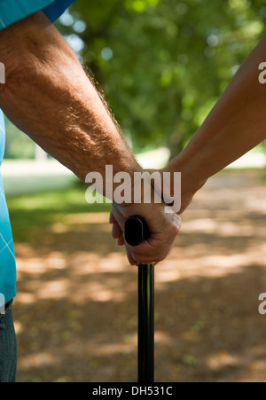 Donna mettendo la sua mano sulla mano di un uomo anziano tenendo un bastone da passeggio Foto Stock