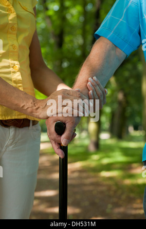 Donna mettendo la sua mano sulla mano di un uomo anziano tenendo un bastone da passeggio Foto Stock