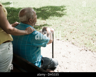 Donne Cercando dopo un anziano uomo seduto su una panchina nel parco Foto Stock