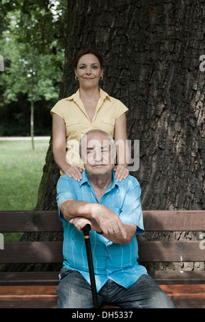 Donne Cercando dopo un anziano uomo seduto su una panchina nel parco Foto Stock