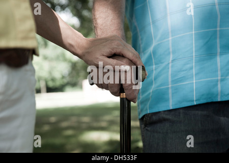 Donna mettendo la sua mano sulla mano di un uomo anziano tenendo un bastone da passeggio Foto Stock