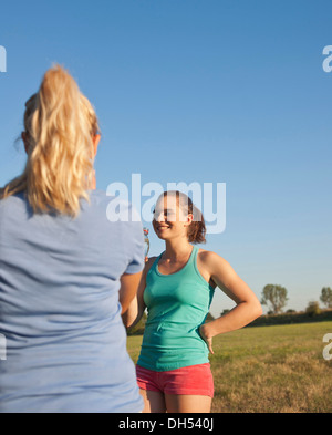 Due giovani donne in piedi in un prato, messa in pausa per un drink mentre si fa sport Foto Stock