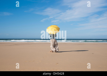 Donna che cammina con un ombrellone in spiaggia Foto Stock