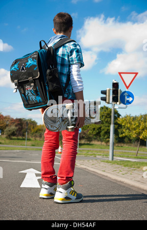 Ragazzo con un sacco di scuola e uno skateboard su una strada Foto Stock