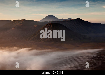 Nebbia di mattina in Tengger Caldera con il monte vulcano Bromo, sinistra Cratere vulcano Batok, anteriore destra, e Gunung Semeru vulcano Foto Stock