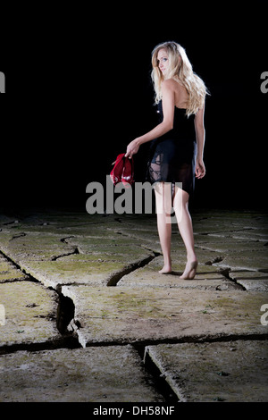 Giovane donna camminare a piedi scalzi in un abito da sera in tutta crepata argilla, Schwaz, Schwaz, distretto Nord Tirolo Tirolo, Austria Foto Stock